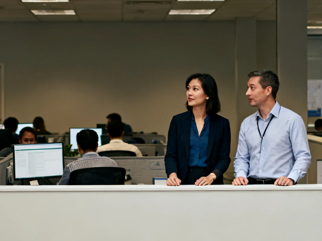 Two professionals discussing workplace needs beside an office partition.